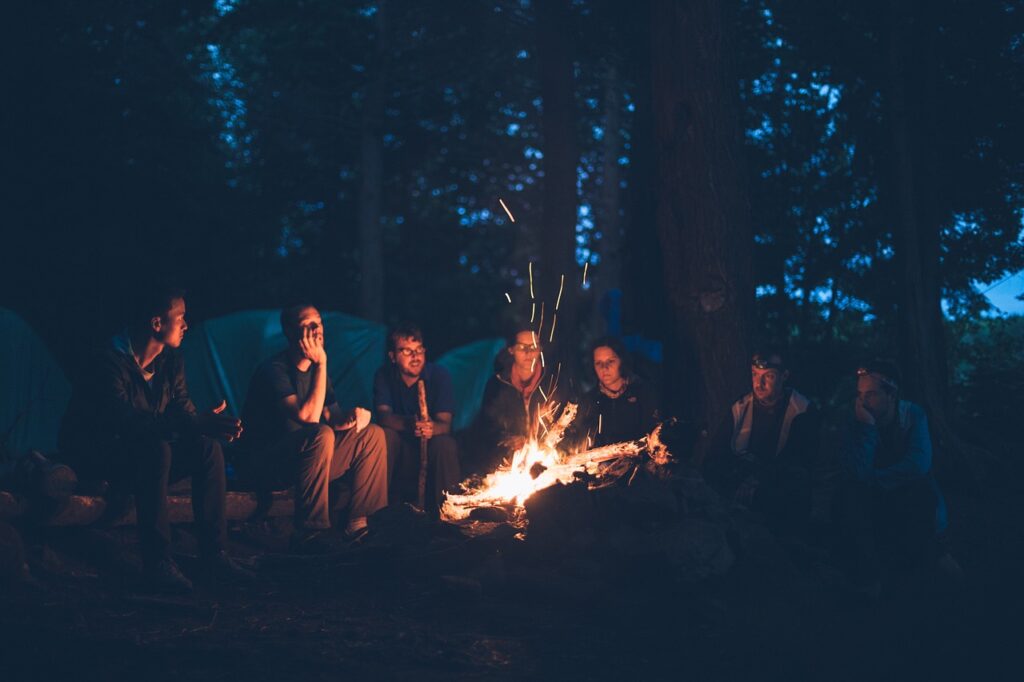 a group of seven young people sitting around a camp fire